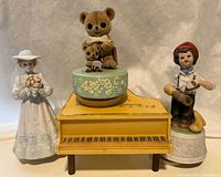 Front view of four Japanese music boxes: bride figurine, fuzzy bear, grand piano, and boy figurine