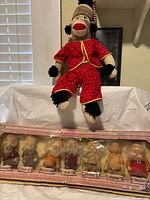 Full view of sock monkey doll in red pajamas seated above boxed dwarfs set