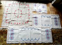 All embroidered textile pieces laid flat together showing the square tablecloth, two runners, and two small mats.