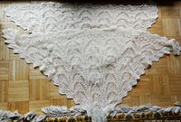 Two hand crocheted Estonian Haapsalu scarves laid flat on parquet floor, showing full triangular shape and scalloped edges.