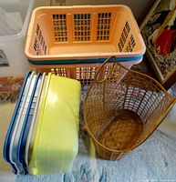 Photo showing three peach and teal plastic laundry baskets stacked inside each other, five dish pans in various colors stacked, and one brown plastic basket standing upright.