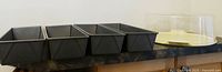 Four rectangular metal load pans and a plastic cake holder with cover on countertop