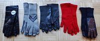 All five pairs of gloves displayed in a row on a floor: two pairs black leather, one pair gray yarn knit, one red yarn knit, and one navy blue yarn knit with brown stripes.