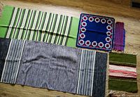 Five woven runners and mats laid flat on a floor, showing various colors and patterns including blue-grey, green wool, and smaller colorful mats.