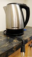 Front angle view of Black & Decker electric kettle on countertop showing stainless steel body, black handle, and power cord.