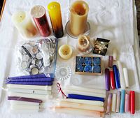 Full view of assorted candles laid out on a white cloth background, showing various sizes and colors including pillar, taper, and tealights along with two glass candle holders.