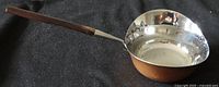 Long view of the copper ladle showing the wooden handle and polished interior bowl