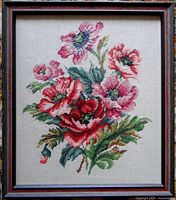 Framed needlepoint artwork showing a bright floral design with glass cover.