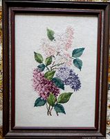 Framed needlepoint of lilacs showing the full artwork and wooden frame.