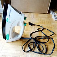 White and black Black & Decker Quick 'n' Easy 360 steam iron with green buttons and knobs, laying on wooden floor with power cord coiled nearby.