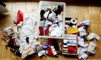 Wide view of assorted laces, crochet pieces, trim bundles, and other sewing supplies inside and around a plastic container on the floor.