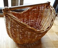 Full view of large light brown woven wicker basket with thick wooden handle showing the basket's shape and weave pattern.