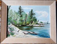 Front view of framed oil painting showing the lake, trees, rocks, and sky with artist signature visible