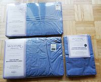 Photo of the twin flat sheet, twin fitted sheet, and a pack of two pillowcases by Signature by Wamsutta in sealed packaging, light blue color.