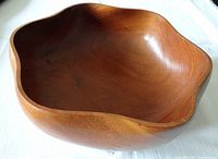 Side view of the teak wood salad bowl showing curved wavy rim and polished wood grain.