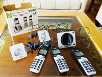 Three VTech cordless handsets, three charging bases, main base station on table with power cords and cables, original box in background