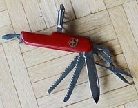 Red vintage Swiss Army multi-tool pocket knife laid out showing blades, scissors, corkscrew, nail file, and bottle opener extended.
