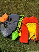 Two youth life jackets laid on grass with plastic toys between them.