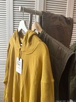 Olive green quilted vest hanging on a rack with additional clothing items nearby, showing overall look and color.
