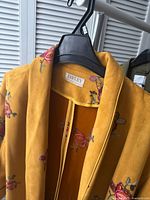 Close-up view of mustard yellow coat on hanger showing Jayley label and floral embroidery on collar and shoulder area.
