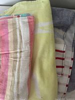 Three folded Lacoste cotton beach towels, showing striped and crocodile graphic designs in pastel colors, yellow, gray and red