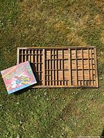 Overall lot including sealed board game box and wooden letter tile tray on grass background