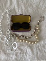 Photo showing the Gucci sunglasses in open case alongside the white plastic chain necklace and two faux pearl necklaces.
