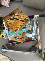 Stacked boxed board games and magic set on top of Razor scooter handlebar and platform in outdoor setting