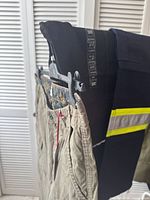 Side view of several folded work pants in dark colors with visible reflective stripes on one pair