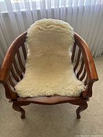Front view showing wooden frame with curved arms and sheepskin throw on the seat and backrest.