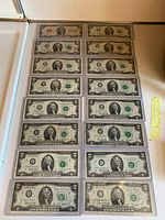 Sixteen US $2 bills arranged in protective sleeves.