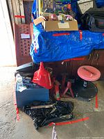 Photo showing entire lot with car ramps leaning against wall, rolling stool in front, multiple tools, and a cardboard box with smaller items on top of a blue tarp covering the ramps.