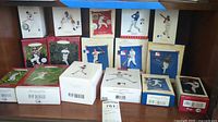 Overview of multiple boxed Hallmark baseball-themed Christmas ornaments arranged on shelf