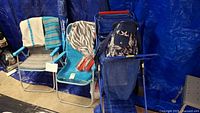 Two beach chairs, one with gray cushion and towels, foldable blue cart with cooler bag and Tommy Bahama umbrella in background