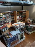 Wide shot of multiple stacks and boxes full of assorted CD jewel cases placed on the floor and shelves.