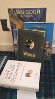 Five coffee table books arranged against a wall including Van Gogh 6 Posters, Moscow, Wicked, Hamburg and The American Heritage Dictionary.
