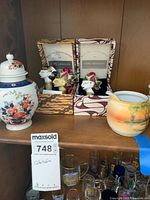 Image showing three Aryaduta bottle stoppers in respective decorative boxes, Japanese ginger jar, and Noritake creamer on shelf.