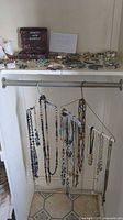 Overview photo of costume jewelry arranged on shelf and hanging from rod, showing variety of necklaces, bracelets, and earrings with decorative ceramic shoes on top shelf.