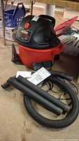 Craftsman 12 gallon wet/dry vacuum unit on floor with flexible hose, two extension wands, and owner's manual.
