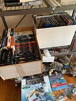 Two cardboard boxes filled with DVDs mostly TV series box sets and some single DVDs, arranged in rows; includes titles such as The Closer, Veronica Mars, Star Wars, and others.