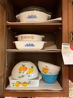 Photo showing three shelves with various glass casserole dishes and mixing bowls in vintage styles, including fruit patterns and cornflower blue flowers.