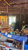 Wide photo of fishing equipment on a blue tarp-covered surface with rods, reels, and accessories in a rustic unfinished room