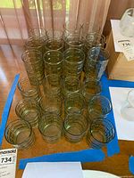 24 vintage drinking glasses with windowpane design in four varying sizes arranged on a table.