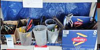 Wide view of multiple containers holding hand tools including pliers and wrenches boxed in Barilla pasta boxes and plastic buckets on a shelf.