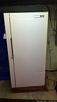 Full view of white Imperial upright freezer showing front door, recessed handle, and power cord in basement setting.