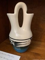Front and angled views of Indigenous American wedding vase showing signature, double spout and handle, and detailed black and blue geometric design on white background.