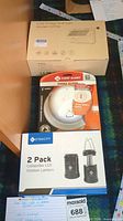 Three items on a carpeted floor: sealed box labeled Solar Energy Wall Light Model CP706, First Alert smoke alarm in packaging, and box showing LED outdoor lanterns branding.