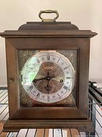 Front view of Hamilton wind up mantle clock showing wooden case, glass door, round clock face with Roman numerals and key winding holes.