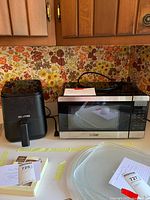 Microwave oven and air fryer placed side by side on a countertop with a floral wallpaper background.