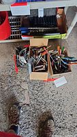 Photo showing two cardboard boxes filled with multiple hand tools including screwdrivers, pliers, and other hand tools resting on the floor.